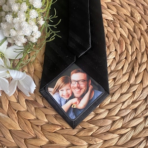 May include: Black tie with a white stripe pattern and a personalized photo insert featuring a father and daughter smiling. The photo insert is in a black frame. The tie has a "croft & barrow" label.