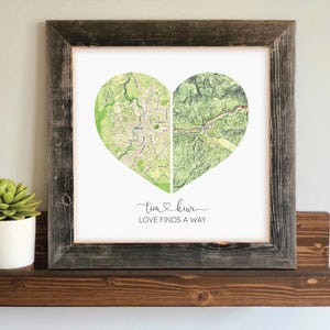 May include: A framed print featuring a heart-shaped map design. The map is split into two sections, with green and white tones. The frame is made of rustic, dark wood. The text "Love Finds a Way" is written below the heart.