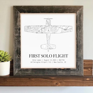 May include: A framed print featuring a detailed black and white airplane map design. The text "FIRST SOLO FLIGHT" is displayed below the plane, along with the pilot's name, date, and airport information. The frame is made of rustic, weathered wood.