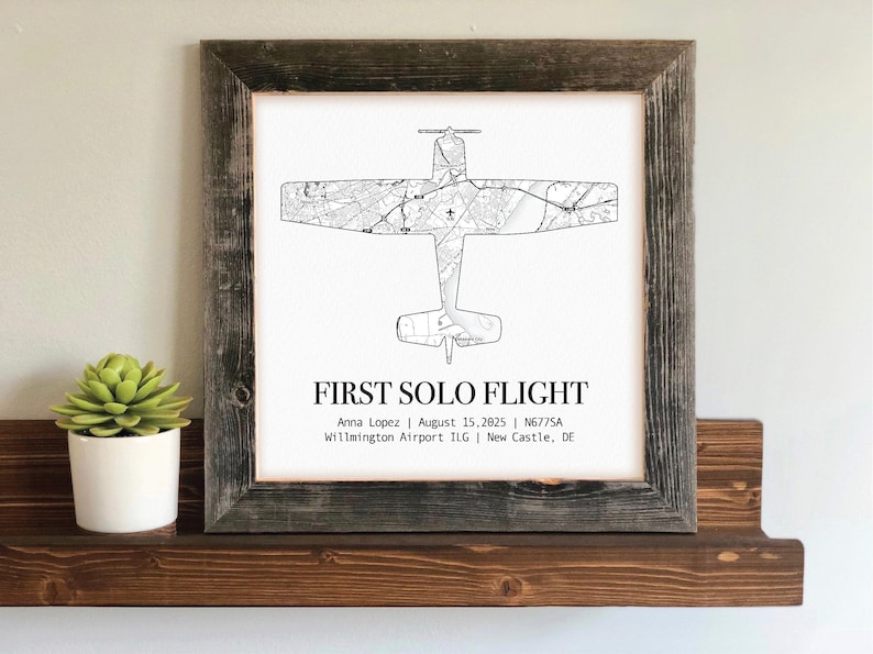 May include: A framed print featuring a detailed black and white airplane map design. The text "FIRST SOLO FLIGHT" is displayed below the plane, along with the pilot's name, date, and airport information. The frame is made of rustic, weathered wood.