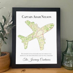 May include: Black framed print with a map design in the shape of an aeroplane. The map is green and white. The text at the top reads "CAPTAIN ADAM NELSON". Below the plane is the text "BE CONFIDENT IN WHATEVER DIRECTION YOU CHOOSE TO GO. The Journey Continues."