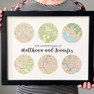 May include: A framed print featuring six circular map illustrations. The maps depict various locations, including Paris, and are arranged around the text "THE ADVENTURES OF Matthew and Jennifer". The frame is black.