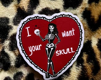 May include: A red heart-shaped sticker with a white border and a skeleton figure holding a skull. The sticker says "I want your skull" in white text.