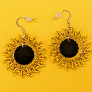 May include: A pair of yellow sunflower earrings with black centres. The earrings are made of acrylic and have a simple silver hook fastening.