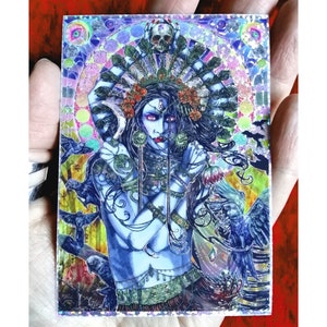 Könnte beinhalten: Detaillierte Illustration einer blauhäutigen Figur mit aufwendigem Kopfschmuck, verziert mit einem Schädel und Federn. Das Kunstwerk zeigt einen mosaikartigen Hintergrund mit leuchtenden Farben und Darstellungen von Vögeln. Die Figur hat dunkles Haar und trägt Schmuck.