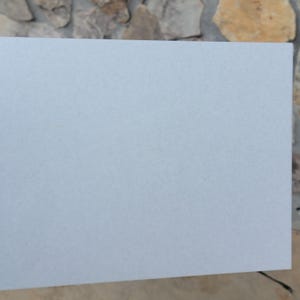 Puede incluir: Un azulejo cuadrado liso de color gris claro con una superficie ligeramente texturizada.