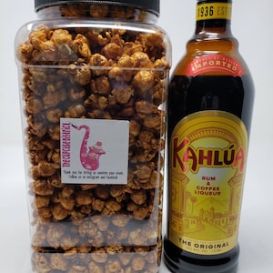 May include: A clear glass jar filled with caramel popcorn and a brown glass bottle of Kahlua coffee liqueur. The bottle has a gold label with the text "Kahlua Rum & Coffee Liqueur The Original" printed on it.