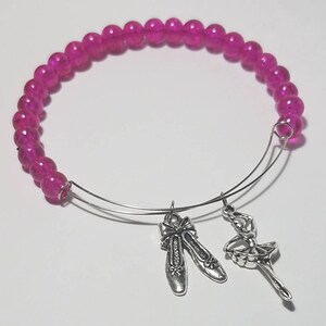 May include: A pink beaded bangle bracelet with silver charms of a ballerina and ballet shoes.