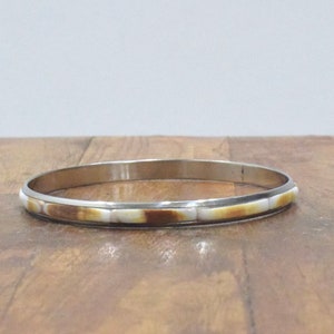 May include: A silver bangle bracelet with a white and brown inlay design.