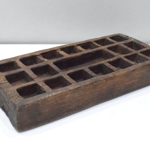 Op de afbeelding: Een rechthoekige houten doos met een raster van vierkante vakken. De doos is gemaakt van donkerbruin hout en heeft een rustieke uitstraling.