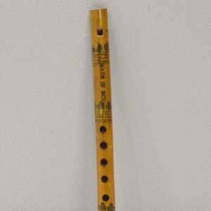 May include: A wooden flute with a natural finish, featuring decorative patterns and the text "MADE IN INDIA". The flute has several finger holes and a red-painted base, showcasing a traditional design.