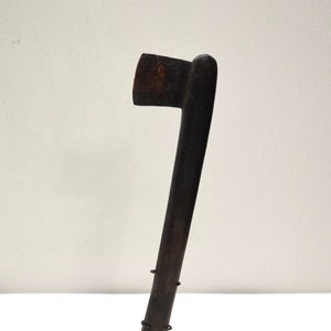 May include: A dark brown wooden axe with a curved handle, mounted on a black metal stand. The axe has a sharp blade and a rounded head.