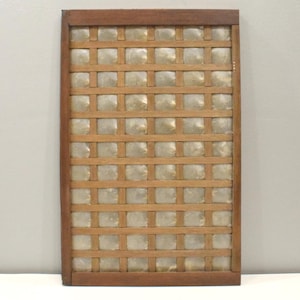 May include: A rectangular wooden frame featuring a grid pattern of thin brown slats. Within each square opening of the grid, a translucent, slightly iridescent, square-shaped shell tile is securely mounted, creating a textured panel design.