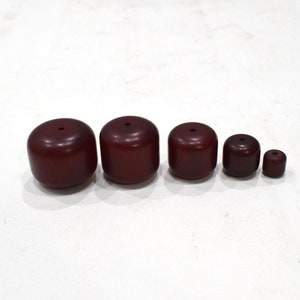 以下が含まれることがあります： さまざまなサイズの木製ビーズが5つあり、すべて濃い赤褐色です。ビーズの中央には小さな穴が開いています。