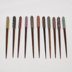 Puede incluir: Doce palitos para el pelo de madera con detalles de cuentas de colores. Los palitos son todos de la misma longitud y tienen un acabado marrón oscuro. Las cuentas están dispuestas en espiral y vienen en una variedad de colores, incluyendo amarillo, rojo, rosa, azul, verde y negro.