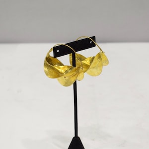 May include: Gold hoop earrings with a unique, twisted design. Each earring is made of multiple overlapping, curved pieces of metal, creating a layered effect.