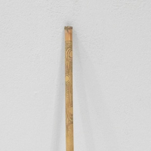 May include: A long, thin, wooden stick with intricate carvings. The stick is light brown in color and has a smooth, polished finish.