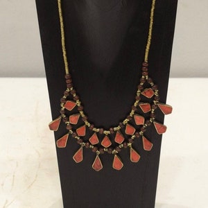 Puede incluir: Un collar de dos niveles con una cadena dorada y colgantes de piedras preciosas rojas. El collar se muestra en un soporte negro.