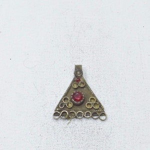 Puede incluir: Un colgante de triángulo de plata con una piedra preciosa roja en el centro y detalles decorativos alrededor de los bordes.