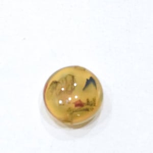 May include: A round, clear glass paperweight with a yellow tint and a black and white image of a landscape inside.