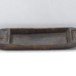 May include: A long, dark brown wooden serving tray with a rectangular inset. The tray has a slightly rounded shape and is carved with simple designs.