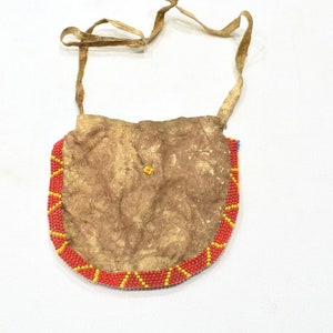 May include: A small, brown leather pouch with a beaded trim. The pouch has a long leather strap and is decorated with red, yellow, and blue beads.
