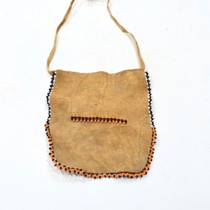 Può includere: Una piccola borsa in pelle marrone con un bordo di perline. La borsa ha una tracolla per il trasporto ed è decorata con perline nere e arancioni.