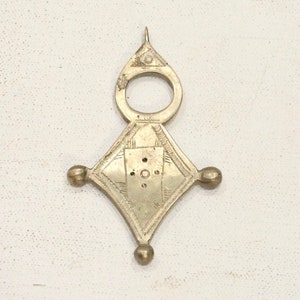 May include: A silver pendant with a diamond shape and a small circle at the top. The pendant has a decorative design with small circles and lines.