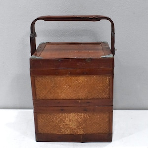 May include: A two-tiered wooden box with a woven bamboo exterior and a brown leather handle. The box has metal accents on the corners and hinges.