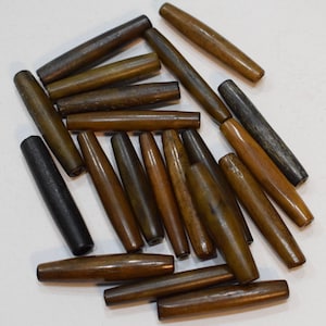 Puede incluir: Una colección de cuentas de madera marrón y negro, algunas con un color marrón oscuro o negro, dispuestas sobre una superficie blanca.