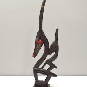 Puede incluir: Una escultura de madera negra de un antílope con cuello largo y cuernos. La escultura está pintada con detalles dorados y rojos y se apoya sobre una base cuadrada.