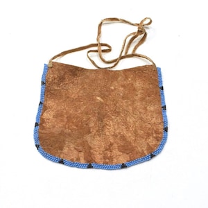Puede incluir: Una bolsa de cuero marrón con un ribete de cuentas azules y negras. La bolsa tiene una correa de cuero para llevar.