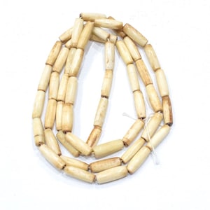 May include: A strand of off-white bone beads, each bead is cylindrical in shape.