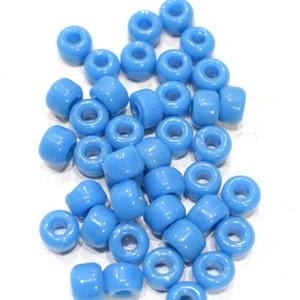 Puede incluir: Un conjunto de cuentas cilíndricas de color azul claro, con un agujero en el centro. Las cuentas están dispersas sobre una superficie blanca, mostrando su textura suave y brillante. Adecuadas para la creación de joyas y manualidades.