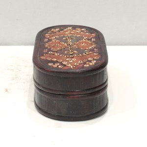 May include: A dark brown wooden box with an oval shape. The top of the box is decorated with a pattern of small, light brown shells.