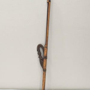 May include: A long, slender, wooden object with a dark, ornate metal piece attached. The wooden portion is light brown, and the metal piece has a curved design. The object appears to be a tool or decorative item.