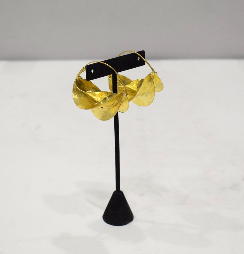 May include: Gold hoop earrings with a unique, twisted design. Each earring is made of multiple overlapping, curved pieces of metal, creating a layered effect.