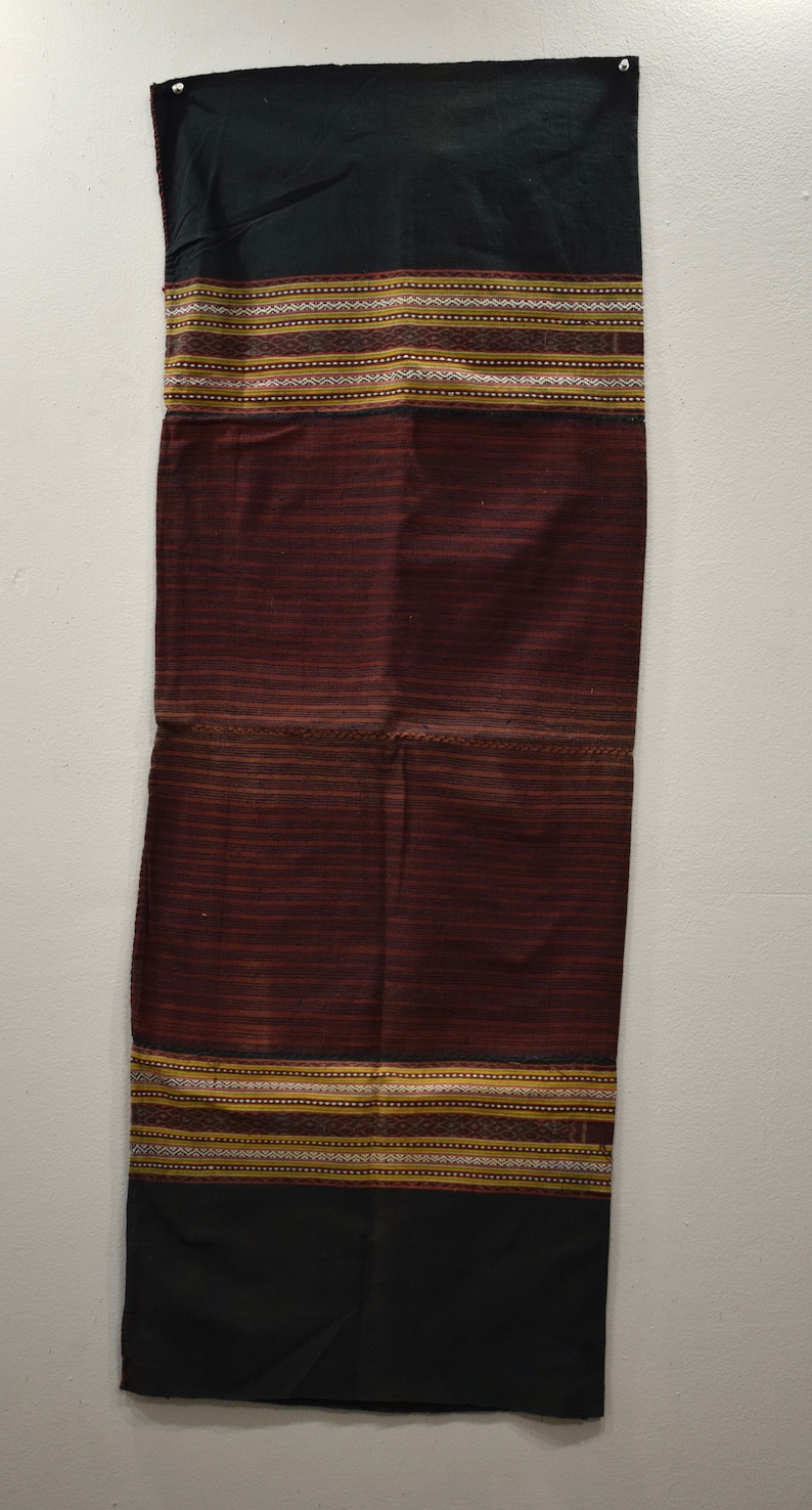 K&ouml;nnte beinhalten: Ein langer, schwarzer und burgunderfarbener Stoff mit komplizierten gewebten Mustern in Gold, Wei&szlig; und Braun. Der Stoff hat eine strukturierte Oberfl&auml;che und ist wahrscheinlich ein traditionelles Textil.