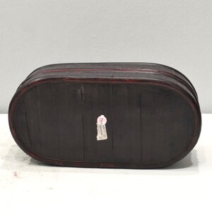 May include: A dark brown oval wooden box with a red rim and a small white label that says "Made in China" on the bottom.