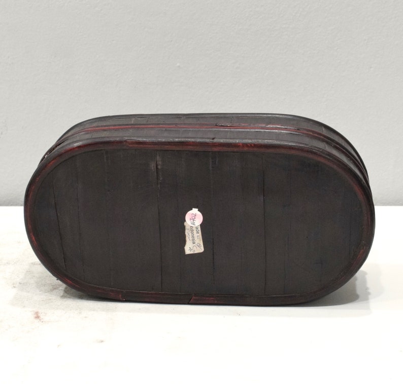 May include: A dark brown oval wooden box with a red rim and a small white label that says "Made in China" on the bottom.