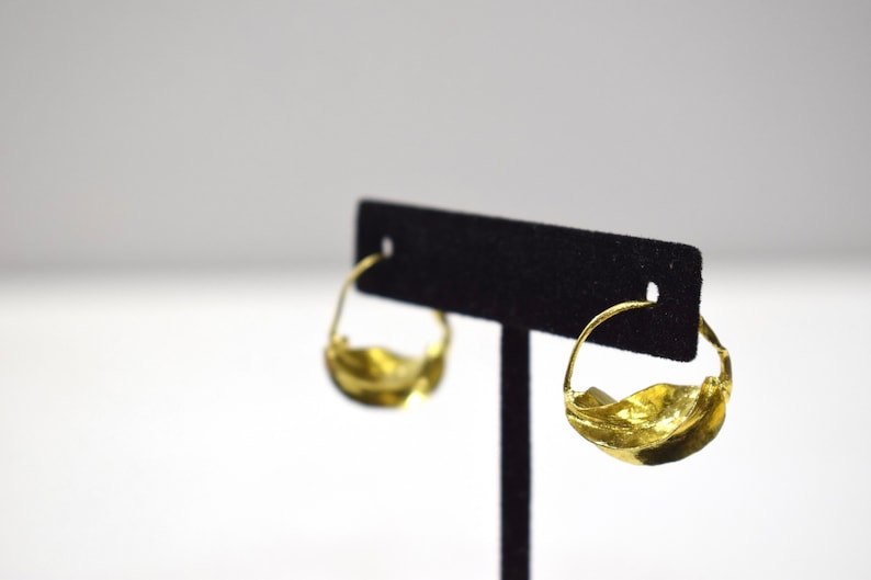 May include: A pair of gold hoop earrings with a wavy, organic design. The earrings are displayed on a black velvet stand.