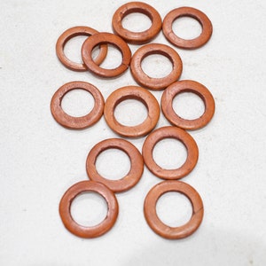 May include: A group of 12 brown wooden rings, scattered on a white surface. The rings are all the same size and shape, and they are made of a smooth, polished wood.