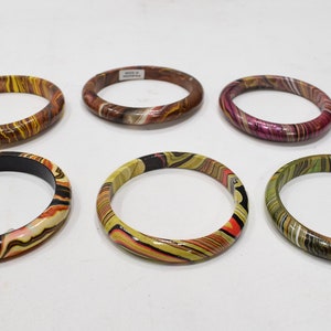 Op de afbeelding: Zes kleurrijke houten armbanden met marmerpatronen. De armbanden zijn gerangschikt in twee rijen van drie. De armbanden zijn allemaal in verschillende kleuren en patronen, waaronder bruin, geel, roze, groen en zwart.