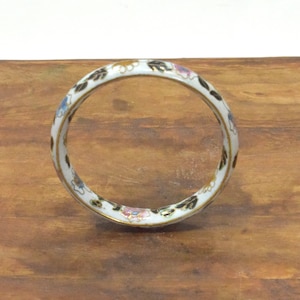 May include: White enamel bangle bracelet with black and gold floral designs.