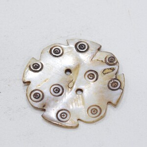 May include: A white mother of pearl button with a decorative design of concentric circles around the edges. The button has a two-hole design.