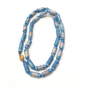 Op de afbeelding: Een blauwe en witte porseleinen ketting met bloemenmotieven. De ketting is gemaakt van cilindrische kralen die aan elkaar geregen zijn met een gouden sluiting.