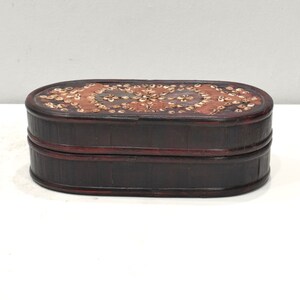 May include: An oval-shaped wooden box with a dark brown finish. The top of the box is decorated with a pattern of small, white shells.