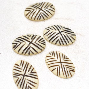 Op de afbeelding: Vijf ovale, witte decoratieve knoppen met een zwart geometrisch patroon. De knoppen hebben een glad, gepolijst oppervlak.
