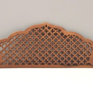 May include: A brown wooden panel featuring an intricate, repeating lattice pattern of small four-pointed star shapes. The panel has a curved, arched top edge and a flat base, showcasing a natural wood grain texture throughout the carved surface.