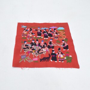 Puede incluir: Un cuadrado textil rojo bordado que presenta una escena detallada de figuras con vestimenta tradicional. Las figuras se representan en varias poses, con acentos coloridos y un gato negro. El bordado está hecho en múltiples colores.